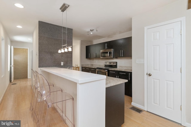 kitchen featuring pendant lighting, a breakfast bar area, light hardwood / wood-style flooring, stainless steel appliances, and kitchen peninsula