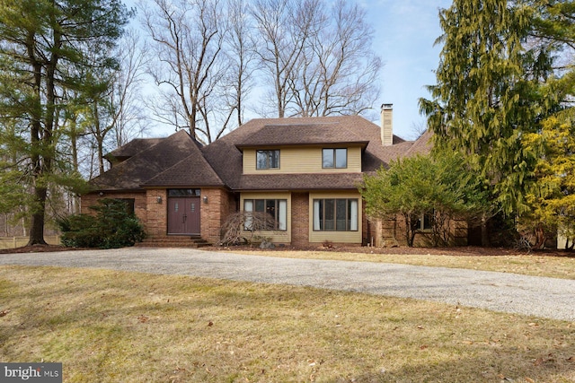 view of front of property with brick siding, a shingled roof, gravel driveway, a front lawn, and a chimney