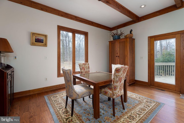 dining room with beamed ceiling, a healthy amount of sunlight, baseboards, and light wood finished floors