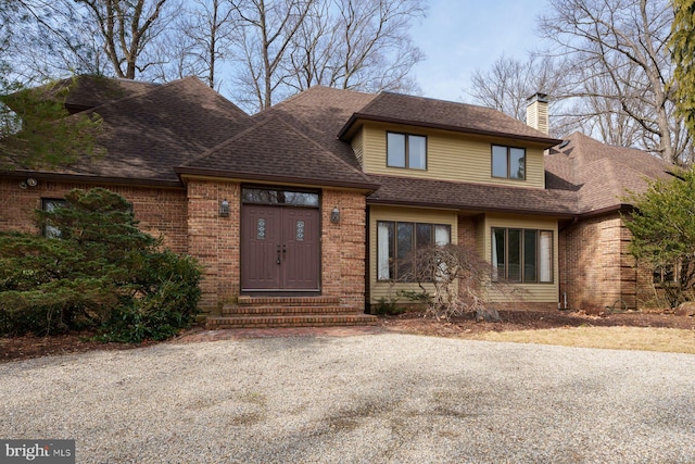 view of front of property featuring brick siding, roof with shingles, and a chimney