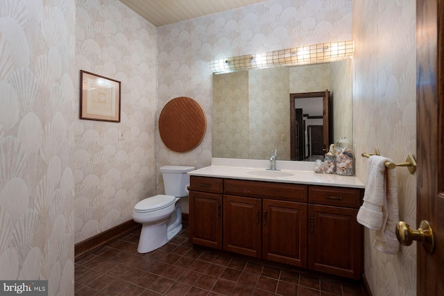 half bath with tile patterned flooring, wallpapered walls, baseboards, toilet, and vanity