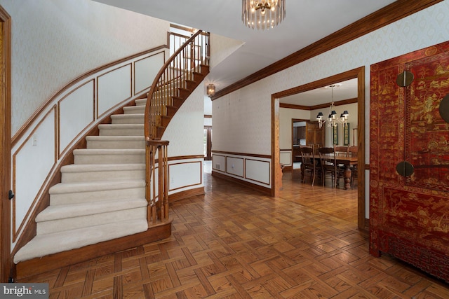 staircase with wallpapered walls, an inviting chandelier, ornamental molding, wainscoting, and a decorative wall