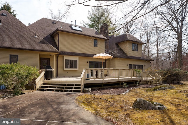 rear view of property with a wooden deck and roof with shingles