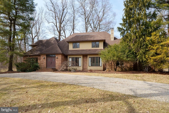 view of front of house featuring aphalt driveway, a chimney, a front yard, and a shingled roof