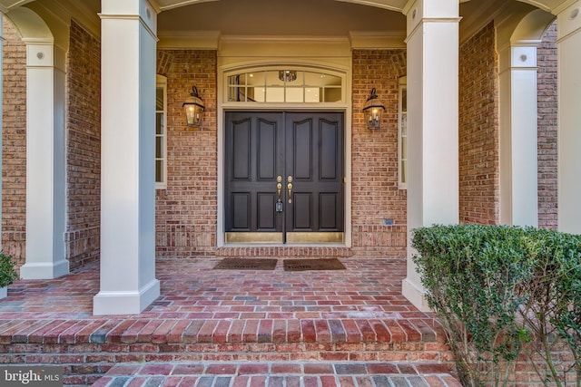 view of exterior entry with a porch and brick siding