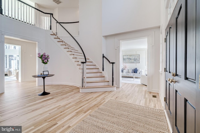 foyer with light wood-style floors, visible vents, a high ceiling, and stairway