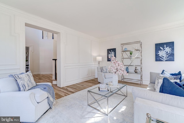 living area featuring crown molding, light wood-style flooring, and a decorative wall