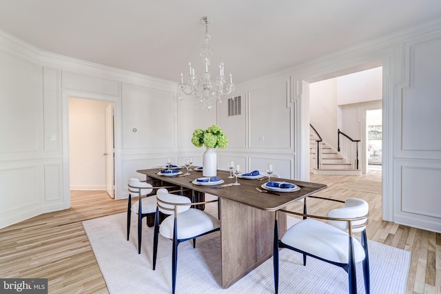 dining area with a decorative wall, visible vents, ornamental molding, stairway, and light wood finished floors