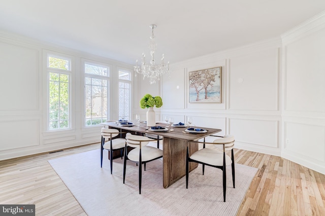 dining space featuring visible vents, crown molding, light wood-type flooring, a chandelier, and a decorative wall