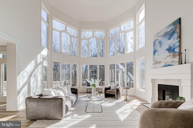 living area featuring light wood-type flooring, a glass covered fireplace, a towering ceiling, and baseboards