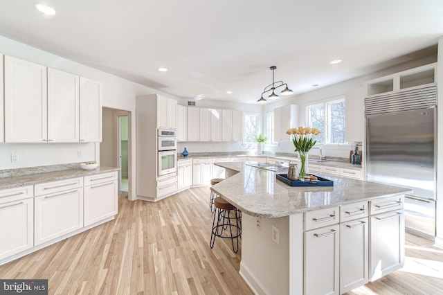 kitchen with white cabinets, a kitchen island, appliances with stainless steel finishes, light stone counters, and hanging light fixtures