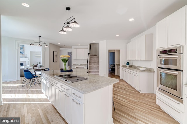 kitchen with stainless steel double oven, light stone countertops, white cabinets, hanging light fixtures, and a center island