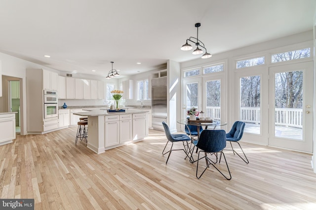 kitchen with light wood-type flooring, a kitchen island, decorative light fixtures, and white cabinets