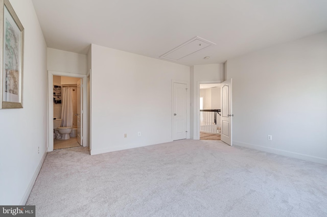 unfurnished bedroom with light carpet, ensuite bath, attic access, and baseboards