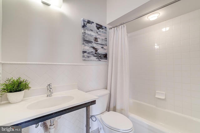 full bathroom with a wainscoted wall, tile walls, toilet, shower / tub combo, and a sink