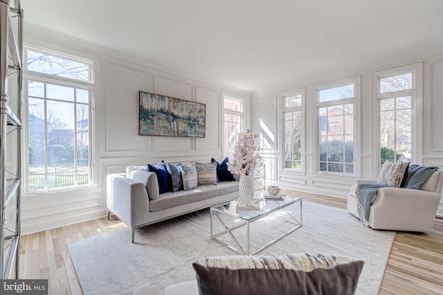 living room featuring ornamental molding, a decorative wall, and light wood-style flooring