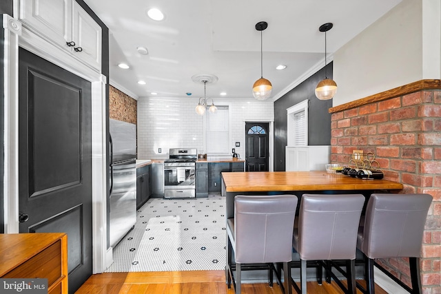 kitchen featuring pendant lighting, butcher block countertops, a breakfast bar area, appliances with stainless steel finishes, and ornamental molding