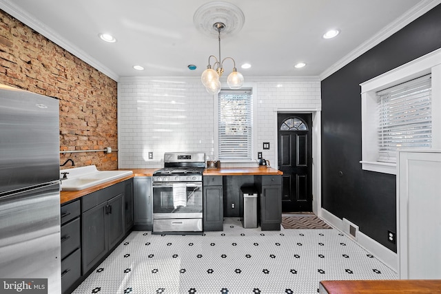 kitchen featuring butcher block counters, sink, crown molding, hanging light fixtures, and stainless steel appliances