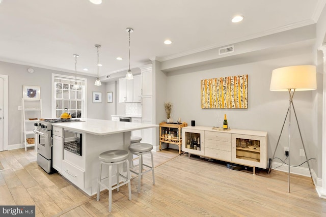 kitchen featuring high end stove, visible vents, white cabinetry, ornamental molding, and light wood finished floors