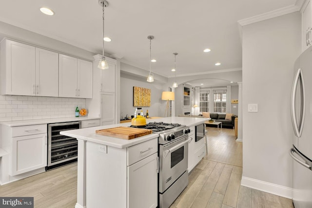 kitchen with arched walkways, beverage cooler, appliances with stainless steel finishes, light wood-type flooring, and decorative backsplash