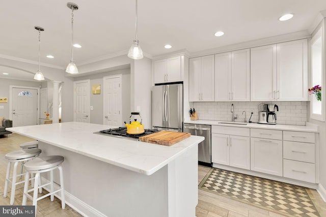 kitchen with appliances with stainless steel finishes, a center island, a sink, white cabinetry, and backsplash