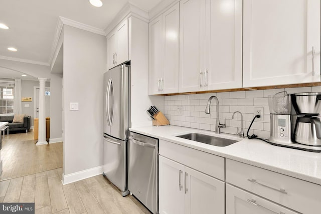 kitchen with a sink, appliances with stainless steel finishes, decorative backsplash, decorative columns, and crown molding