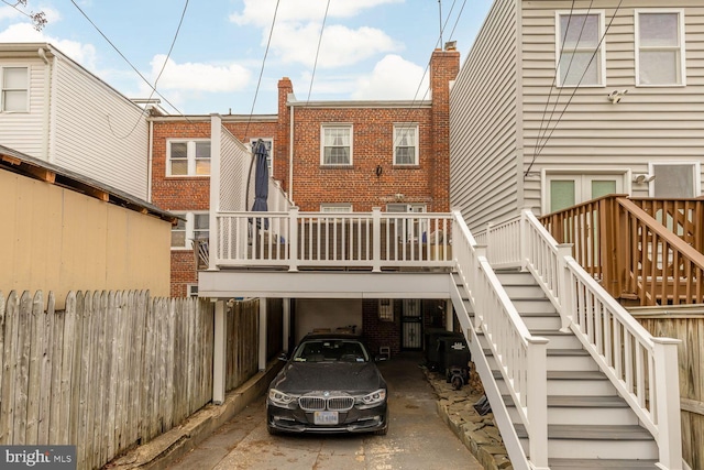 rear view of property with concrete driveway, brick siding, stairway, and fence