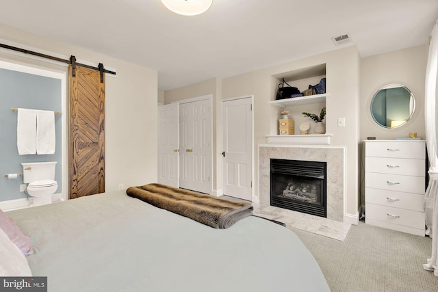 bedroom with a barn door, a fireplace, carpet flooring, visible vents, and ensuite bath