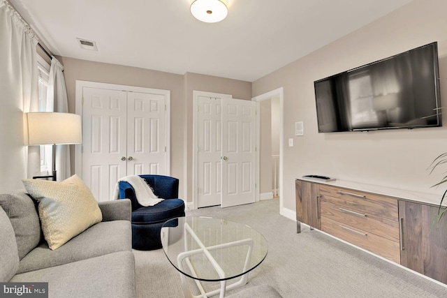 living area featuring baseboards, visible vents, and light colored carpet