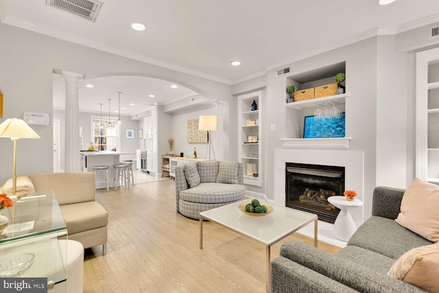 living room featuring ornate columns, visible vents, light wood finished floors, and built in features