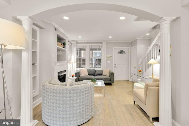 living room with arched walkways, ornamental molding, light wood-style flooring, and ornate columns