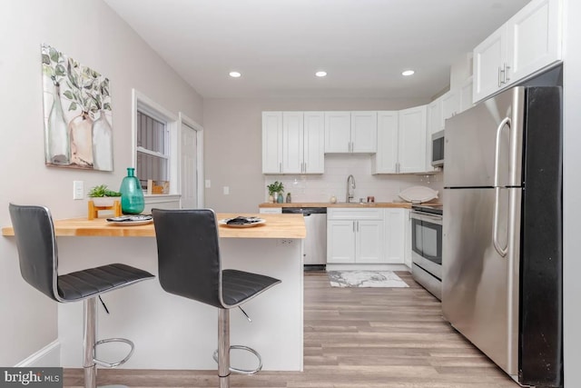 kitchen featuring butcher block counters, a breakfast bar, white cabinets, and appliances with stainless steel finishes