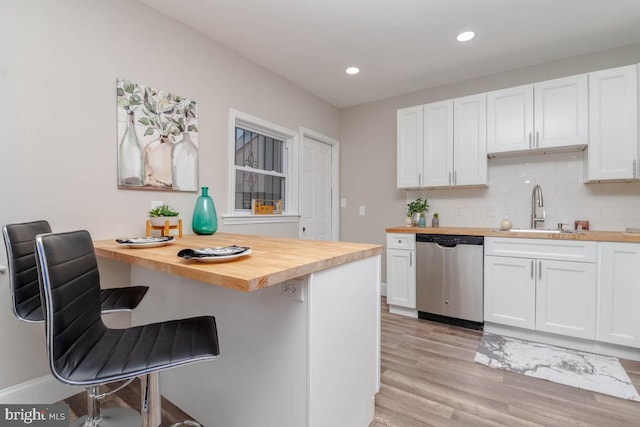 kitchen featuring butcher block counters, sink, a breakfast bar area, stainless steel dishwasher, and white cabinets