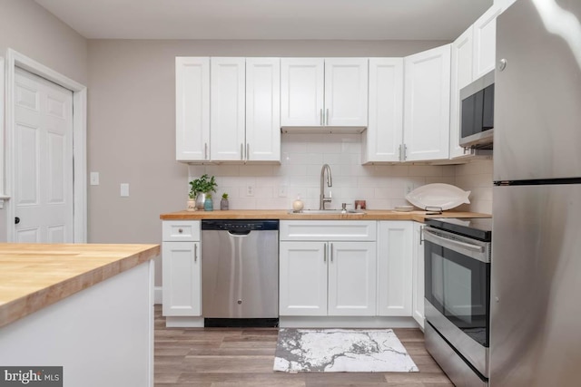 kitchen with butcher block countertops, sink, appliances with stainless steel finishes, white cabinets, and backsplash