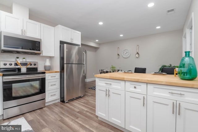 kitchen with wood counters, white cabinetry, stainless steel appliances, light hardwood / wood-style floors, and backsplash