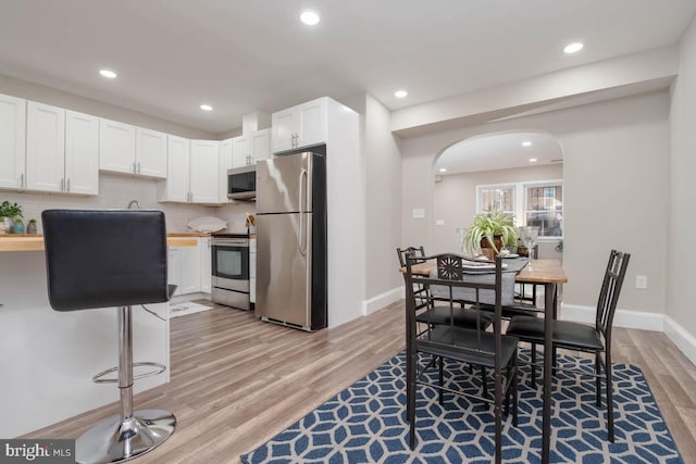 kitchen featuring butcher block countertops, light hardwood / wood-style flooring, appliances with stainless steel finishes, white cabinets, and decorative backsplash