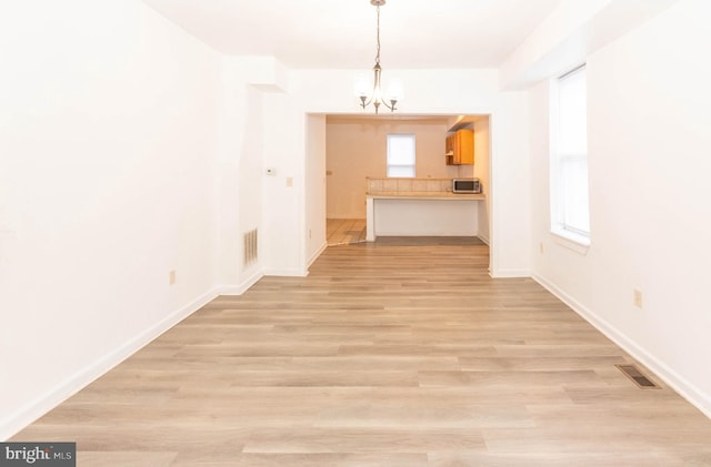 unfurnished living room with an inviting chandelier and light wood-type flooring