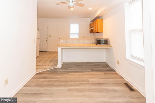 kitchen featuring a kitchen bar, light brown cabinets, light wood-type flooring, kitchen peninsula, and white fridge