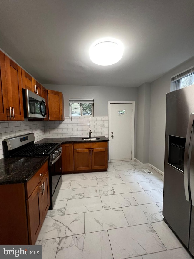 kitchen featuring sink, appliances with stainless steel finishes, tasteful backsplash, a wealth of natural light, and dark stone counters