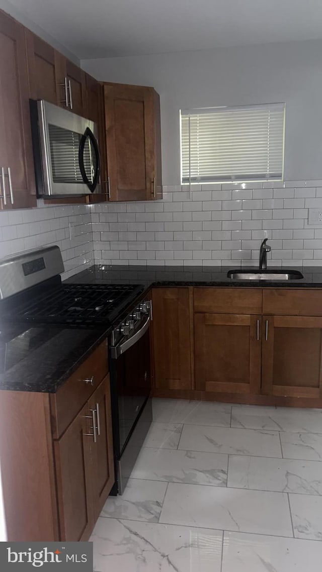 kitchen featuring tasteful backsplash, dark stone countertops, sink, and black gas range oven