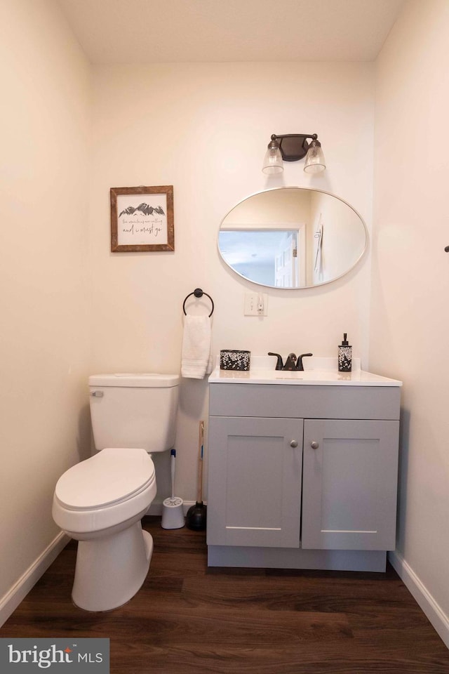 half bathroom featuring baseboards, vanity, toilet, and wood finished floors