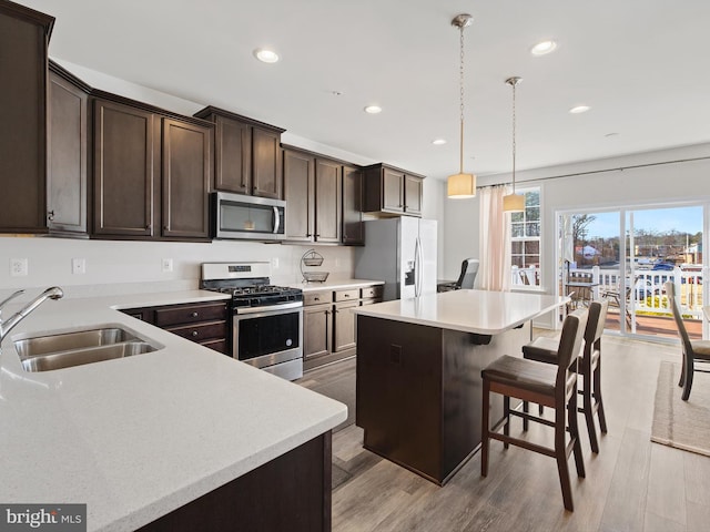 kitchen featuring appliances with stainless steel finishes, hanging light fixtures, a kitchen island, sink, and a kitchen bar