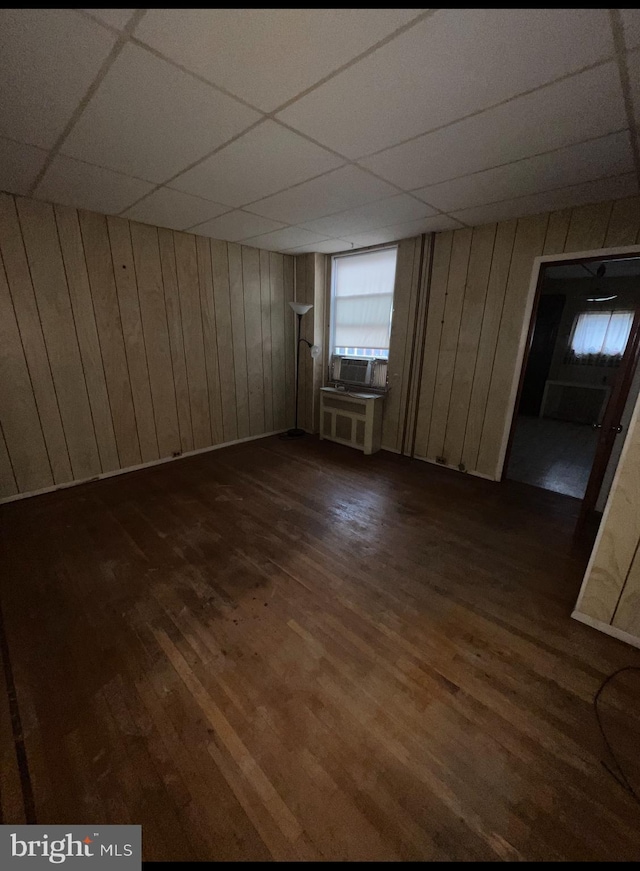 unfurnished room with dark hardwood / wood-style flooring, wooden walls, and a drop ceiling