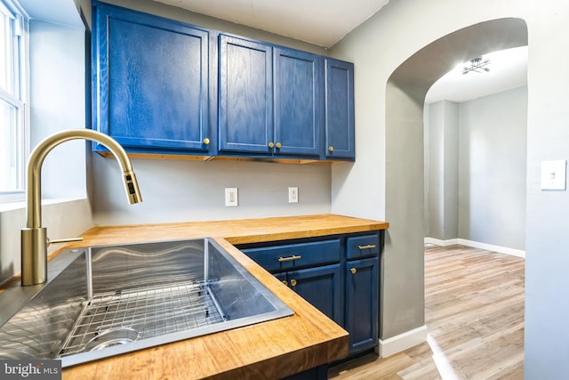 kitchen with sink, light hardwood / wood-style floors, blue cabinets, and wood counters