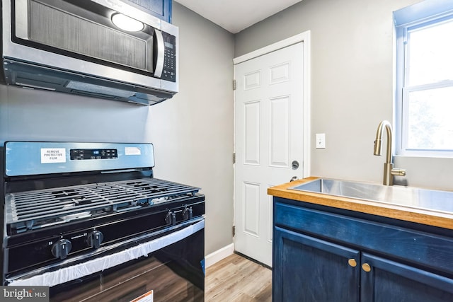 kitchen with sink, gas range, blue cabinets, and light hardwood / wood-style floors