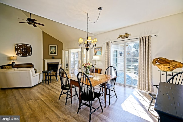 dining room with lofted ceiling, wood finished floors, a fireplace, and ceiling fan with notable chandelier