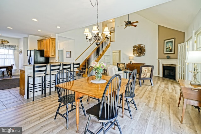 dining room featuring recessed lighting, a fireplace, stairs, light wood-style floors, and ceiling fan with notable chandelier