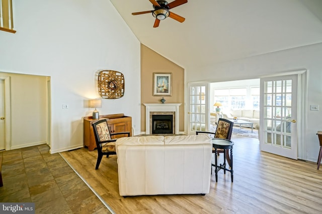 living room featuring high vaulted ceiling, a ceiling fan, wood finished floors, a fireplace, and baseboards