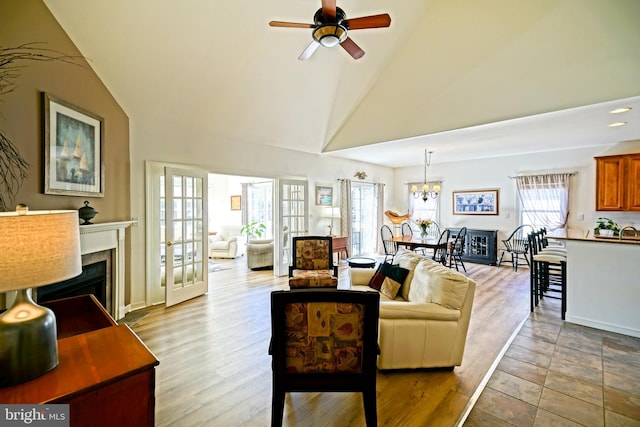 living area with ceiling fan with notable chandelier, wood finished floors, a fireplace, and high vaulted ceiling