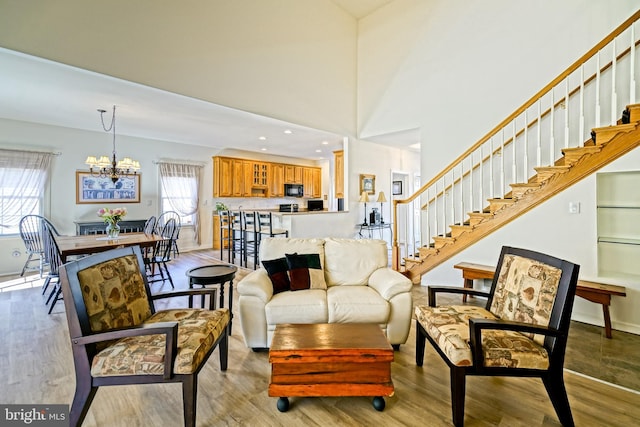 living room with a notable chandelier, stairs, light wood-type flooring, and baseboards